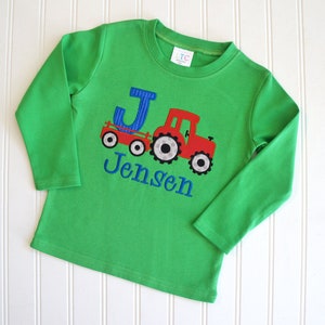 May include: Green long-sleeved shirt with a red tractor and blue letter J, personalized with the name "Jensen".