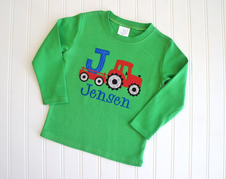 May include: Green long-sleeved shirt with a red tractor and blue letter J, personalized with the name "Jensen".