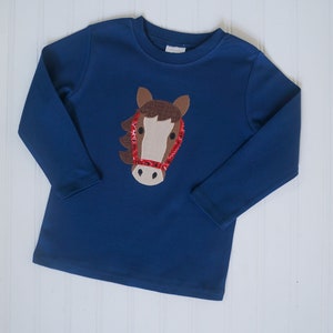 May include: A blue long-sleeved shirt with a brown horse head applique. The horse has a red sequined bridle.