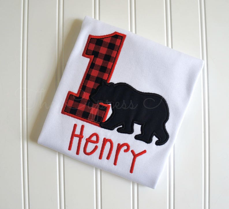 May include: White onesie with a red and black plaid number one, a black bear silhouette, and the name "Henry" embroidered in red.