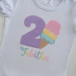 May include: White t-shirt with a purple number two with white polka dots, a multi-colored ice cream cone, and the name Tabitha in rainbow colors.