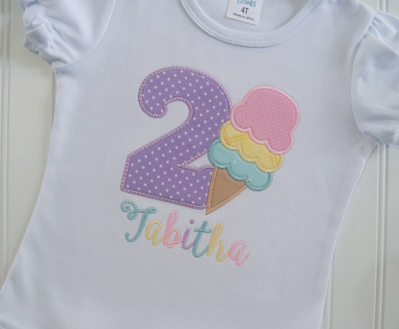 May include: White t-shirt with a purple number two with white polka dots, a multi-colored ice cream cone, and the name Tabitha in rainbow colors.