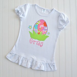 May include: White t-shirt with a colorful Easter egg design and the name "Gray" embroidered on the front.