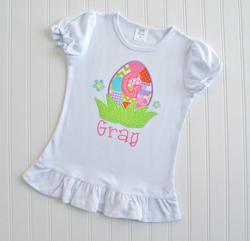 May include: White t-shirt with a colorful Easter egg design and the name "Gray" embroidered on the front.