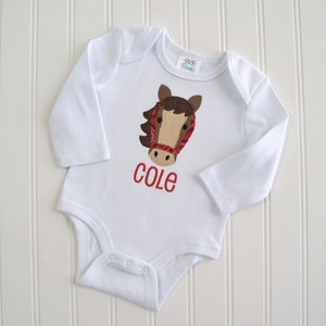 May include: White long-sleeved baby onesie with a brown horse head applique and the name "COLE" embroidered in red.