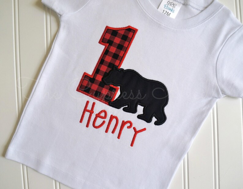 May include: White t-shirt with a red and black buffalo plaid number one, a black bear silhouette, and the name "Henry" embroidered in red.