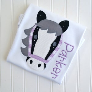 May include: White t-shirt with a gray and black horse head applique and the name "Parker" embroidered in purple.