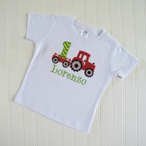 May include: White t-shirt with a red tractor and a green number one on it. The name Lorenzo is embroidered in green below the tractor.
