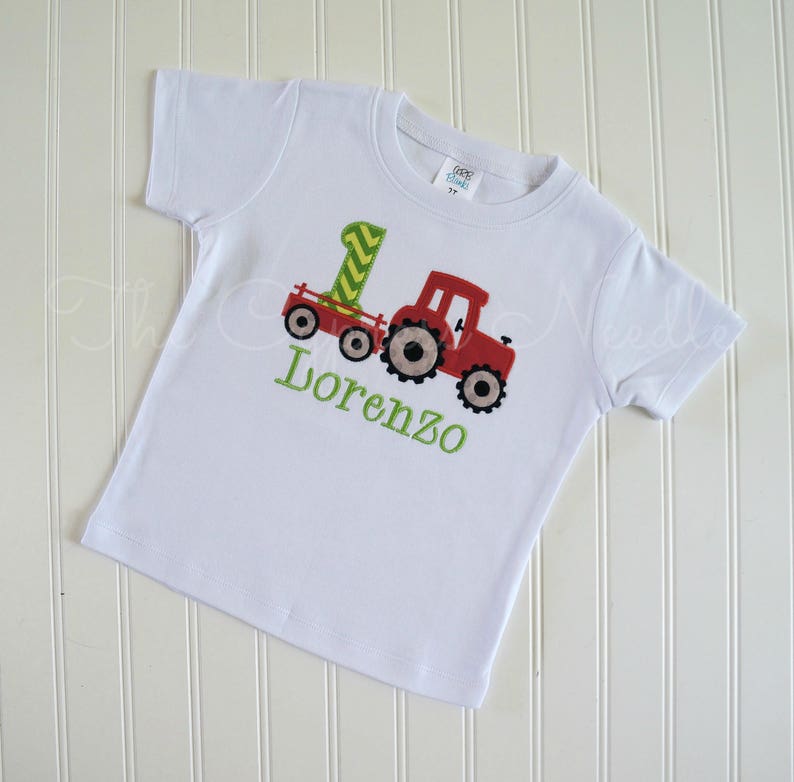 May include: White t-shirt with a red tractor and a green number one on it. The name Lorenzo is embroidered in green below the tractor.