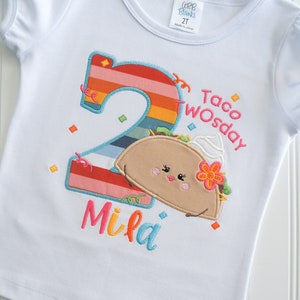 May include: White t-shirt with a rainbow number two, a cartoon taco with a flower and the text "Taco Twosday" and the name "Mila" embroidered on it.