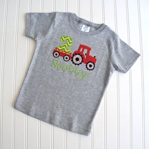 May include: Gray short-sleeved t-shirt with a red tractor pulling a wagon with a green number 2 on it. The text "Scotty" is embroidered in green below the tractor.