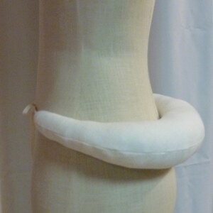 May include: A white fabric cushion shaped like a crescent moon. The cushion is tied with a thin beige ribbon.
