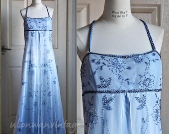 May include: A light blue formal gown with spaghetti straps and a flowing skirt. The bodice and straps are embellished with dark blue beading and floral embroidery. The dress is displayed on a mannequin.