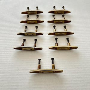 Könnte beinhalten: Zehn antike Messing-Schrankknöpfe mit einem cremefarbenen ovalen Einsatz und einem schlichten Design. Jeder Knopf hat zwei schwarze Schrauben.