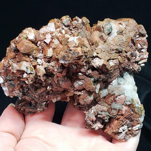 May include: A natural mineral specimen featuring a cluster of reddish-brown crystals with a layered, textured appearance. The crystals have a rough, irregular shape and are interspersed with lighter-colored, crystalline formations. The overall structure is complex and visually striking.
