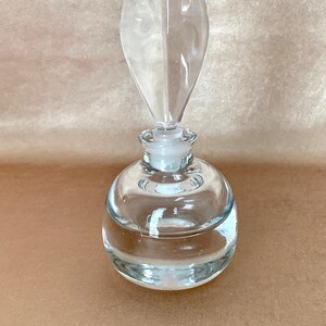 May include: A clear glass bottle with a unique, pointed stopper. The bottle has a round body and a textured surface.