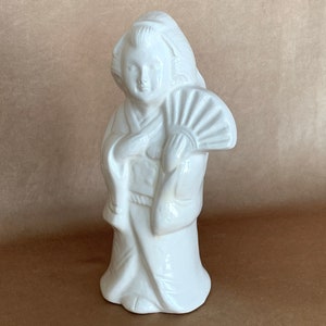 May include: White ceramic figurine of a woman in a traditional Japanese kimono holding a fan.