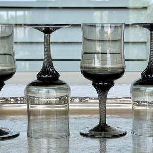 May include: Four clear glass wine glasses with a twisted stem and a dark gray tint. The glasses are arranged in a row on a silver tray.