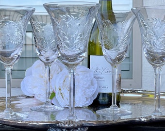May include: Five clear crystal wine glasses with etched floral designs sit on a silver tray with a bottle of white wine in the center. The bottle label reads "The Y Series, Viognier, South Australia, UMBA."