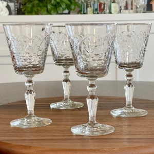May include: Four clear glass wine glasses with a cut glass design. The glasses have a round bowl and a tall, slender stem.
