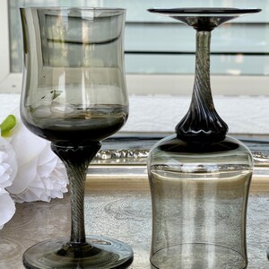 May include: Two clear glass wine glasses with a dark gray tint and a twisted stem. The glasses are on a silver tray.