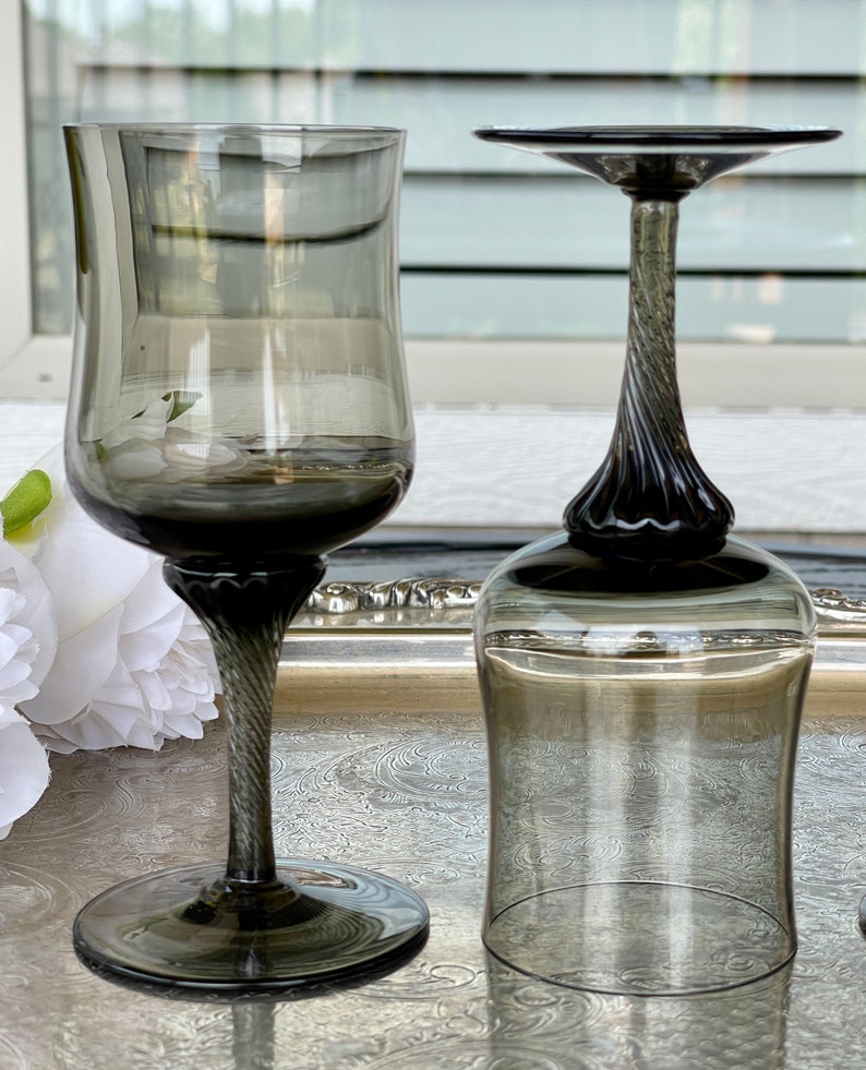 May include: Two clear glass wine glasses with a dark gray tint and a twisted stem. The glasses are on a silver tray.