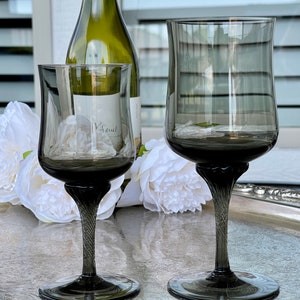 May include: Two dark gray glass wine glasses with a twisted stem on a silver tray with white flowers. The larger glass is taller and wider than the smaller glass.