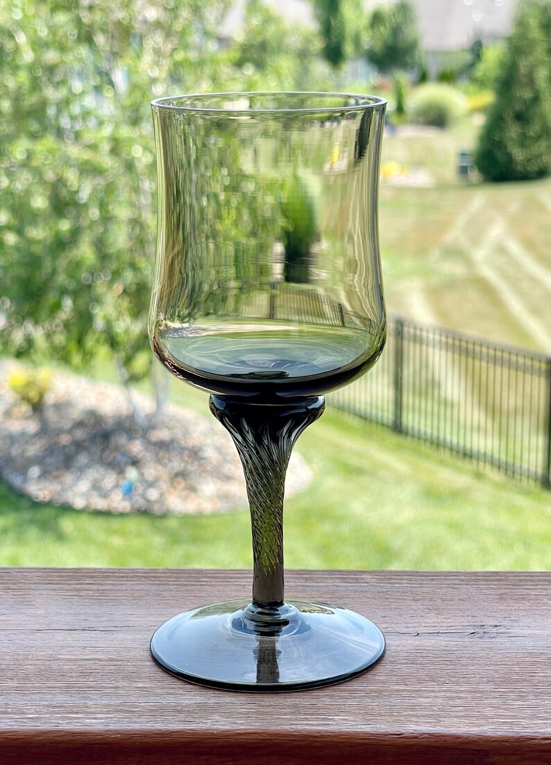 May include: A dark gray glass wine glass with a twisted stem. The glass is empty and has a rounded bowl.