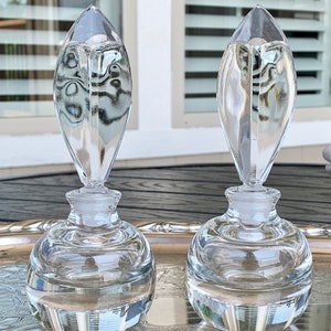 May include: Two clear glass perfume bottles with a teardrop-shaped stopper. The bottles are sitting on a silver tray.