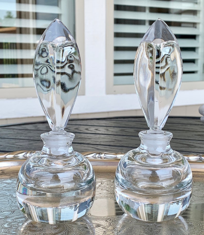 May include: Two clear glass perfume bottles with a teardrop-shaped stopper. The bottles are sitting on a silver tray.