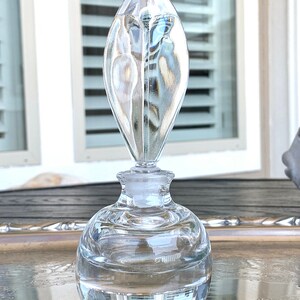 May include: A clear glass bottle with a round body and a tall, pointed stopper. The bottle is sitting on a silver tray.