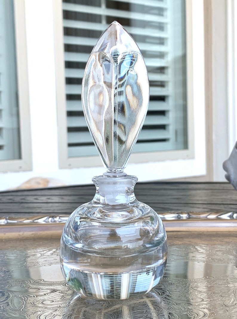 May include: A clear glass bottle with a round body and a tall, pointed stopper. The bottle is sitting on a silver tray.