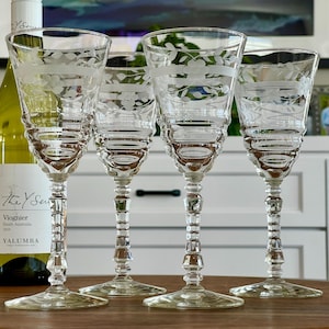 May include: Set of four clear glass wine glasses with etched floral designs. The glasses have a tall, slender stem and a wide bowl.