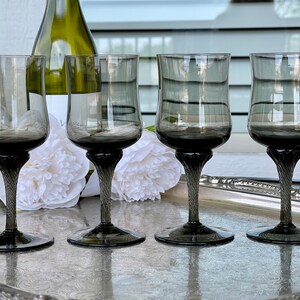 May include: Four clear glass wine glasses with a dark gray tint and a twisted stem. The glasses are arranged in a row on a silver tray.