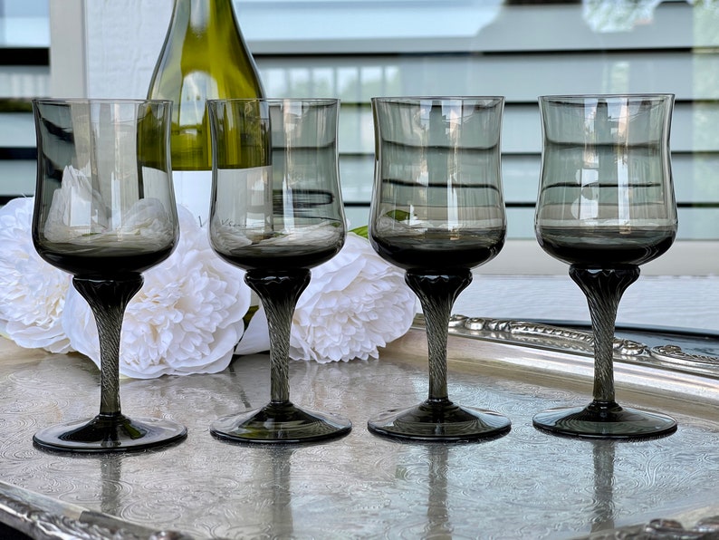 May include: Four clear glass wine glasses with a dark gray tint and a twisted stem. The glasses are arranged in a row on a silver tray.