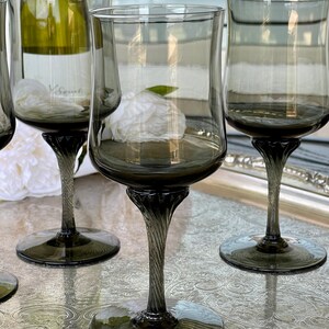 May include: Set of four dark gray glass wine glasses with a twisted stem. The glasses are on a silver tray with an ornate design.