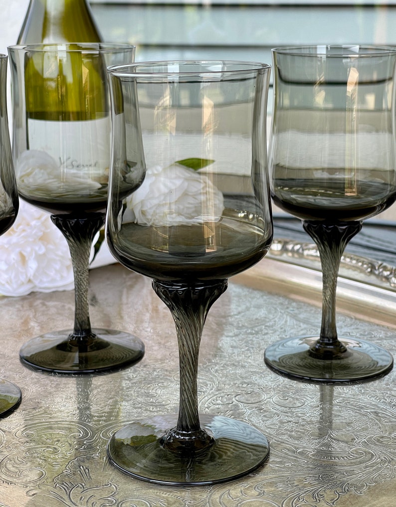 May include: Set of four dark gray glass wine glasses with a twisted stem. The glasses are on a silver tray with an ornate design.