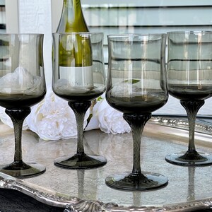 May include: Set of four dark gray glass wine glasses with a twisted stem. The glasses are on a silver tray with white flowers.