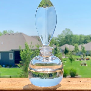 May include: A clear glass bottle with a pointed stopper. The bottle is round and has a textured surface. The bottle is sitting on a wooden surface.