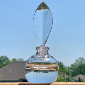 May include: A clear glass bottle with a unique, pointed stopper. The bottle is round and has a slight curve at the bottom. The bottle is filled with a clear liquid.