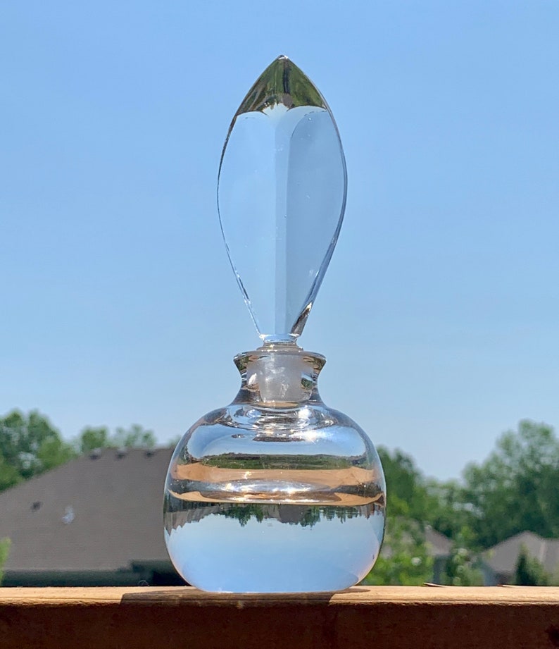 May include: A clear glass bottle with a unique, pointed stopper. The bottle is round and has a slight curve at the bottom. The bottle is filled with a clear liquid.