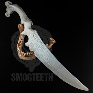 May include: A white, stylized dagger with a textured blade and handle, featuring an antler-like design. The dagger is mounted on a brown jawbone against a black background. The text "SMOGTEETH" is visible.