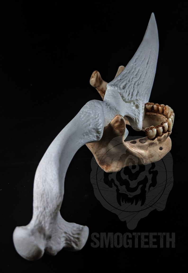 May include: A detailed, off-white sculpture of a stylized bone structure, featuring a curved bone, a jaw with teeth, and a large, blade-like projection. The sculpture is set against a black background, with the text "SMOGTEETH" visible.
