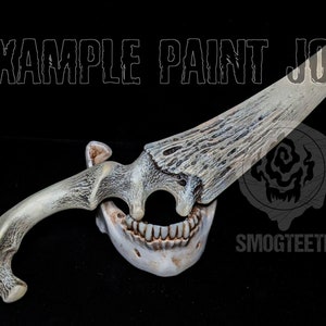 May include: A bone-colored dagger with a blade and handle designed to resemble an antler. The handle is connected to a jawbone with teeth. The text "EXAMPLE PAINT JOB" and "SMOGTEETH" are visible.