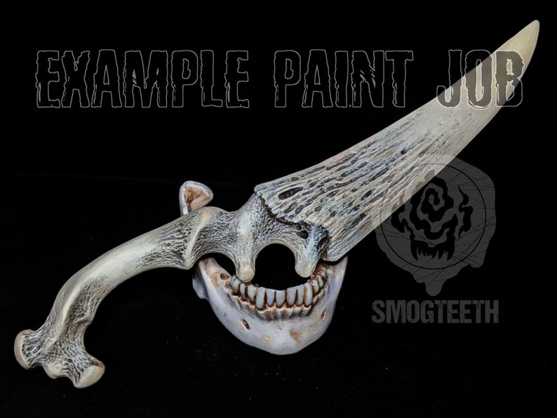 May include: A bone-colored dagger with a blade and handle designed to resemble an antler. The handle is connected to a jawbone with teeth. The text "EXAMPLE PAINT JOB" and "SMOGTEETH" are visible.
