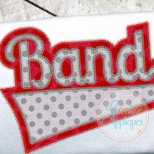 May include: Red and gray applique with the word "Band" in a white outline. The applique is in the shape of a banner with a polka dot pattern.