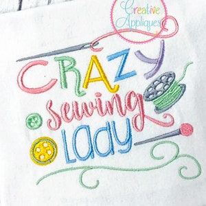 Pode incluir: Desenho bordado em um fundo de tecido branco. O desenho diz "Crazy Sewing Lady" com fio colorido e inclui uma agulha, um carretel de fio e um botão.