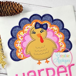May include: A pink and orange turkey with a blue bow on its head. The turkey is embroidered on a white shirt with the name "Harper" in pink letters below it.