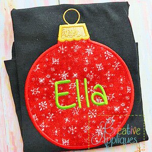 May include: Red Christmas ornament with white snowflakes and the name "Ella" embroidered in green on a black t-shirt.