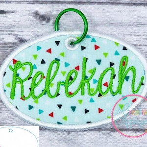 May include: A white oval-shaped fabric patch with a green satin stitched name "Rebekah" on a blue background with colorful confetti. The patch has a green ring attached to it.